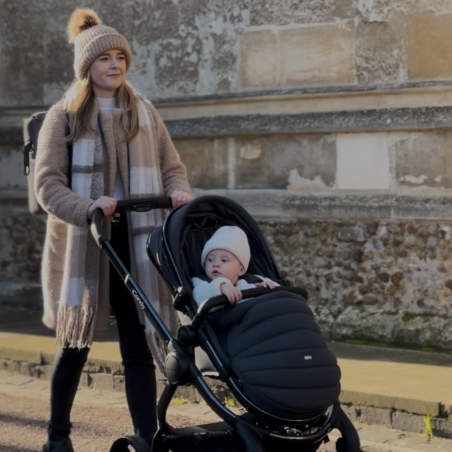 iCandyPeach 7 Black Edition in stroller world facing mode with mom pushing her baby who is in the matching winter footmuff